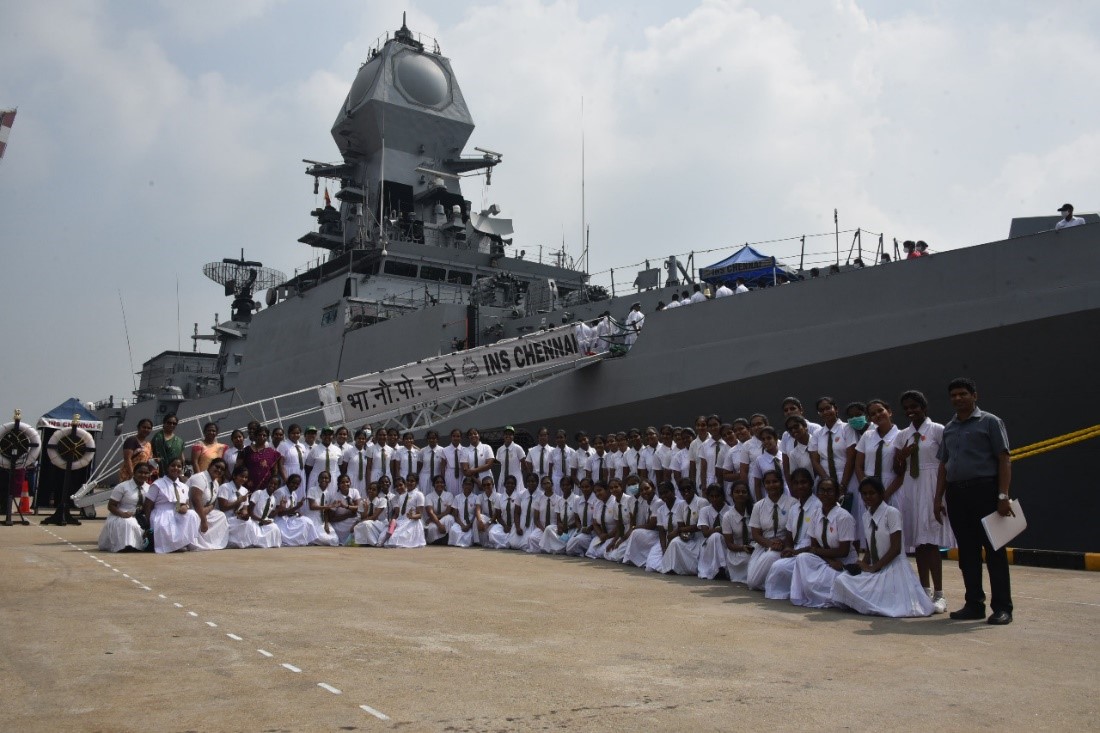 A large group of people in a line in front of a military shipDescription automatically generated with low confidence