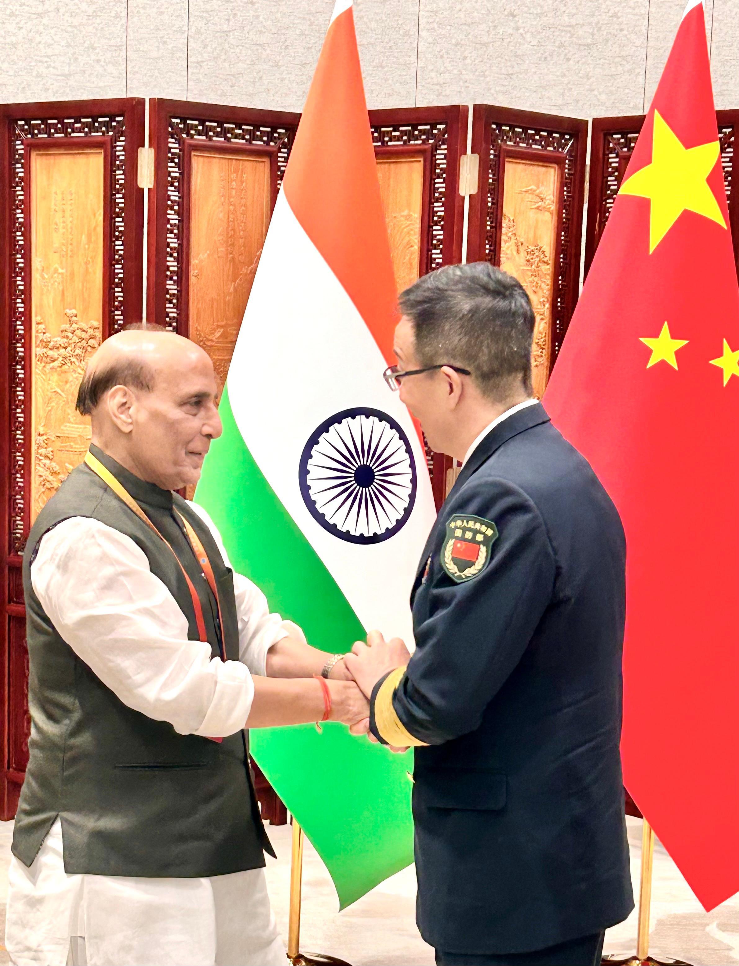 Two men shaking hands in front of flagsDescription automatically generated