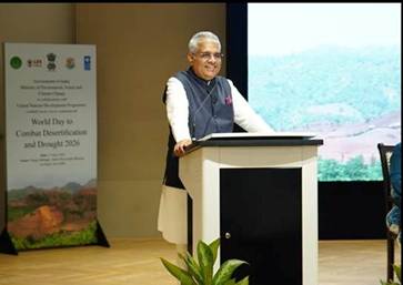 A person in a suit stands at a podium, speaking in front of a podium, with a backdrop showing a scenic landscape and a banner for an environmental event.AI-generated content may be incorrect.