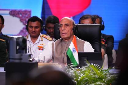 A person sitting at a desk with a flag behind himDescription automatically generated