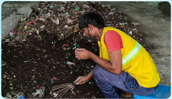 A person in a yellow vest kneeling in a pile of trashDescription automatically generated