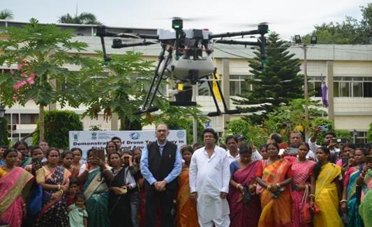 A group of people standing around a drone flyingDescription automatically generated