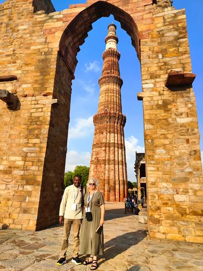 A person and person standing in front of a tall brick tower with Qutub Minar in the backgroundDescription automatically generated